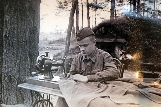 Боец-портной гвардейской стрелковой дивизии за работой на швейной машинке на передовых позициях. 1942 год.