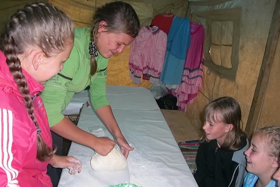Девчата месят тесто для пирогов, которые будут печь на углях от костра.